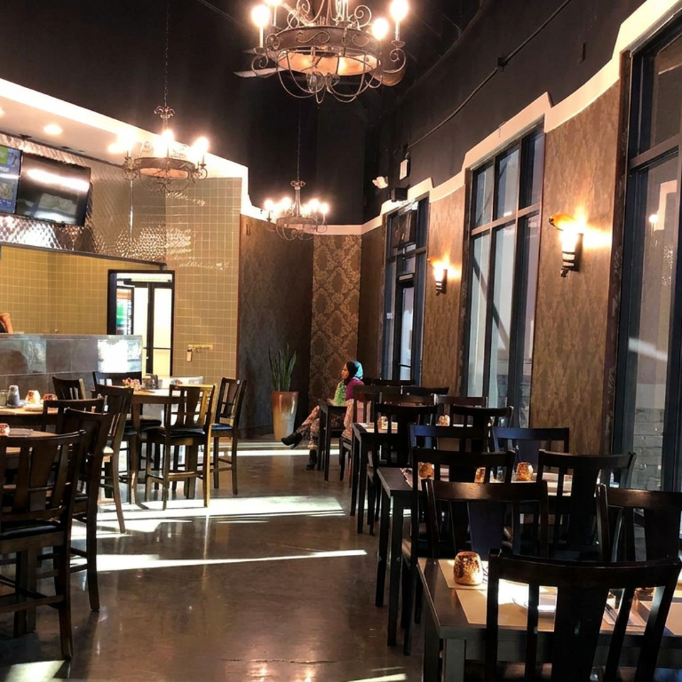 Elegant restaurant dining room with dark wood tables, chandeliers, patterned walls, large windows, and an open kitchen.