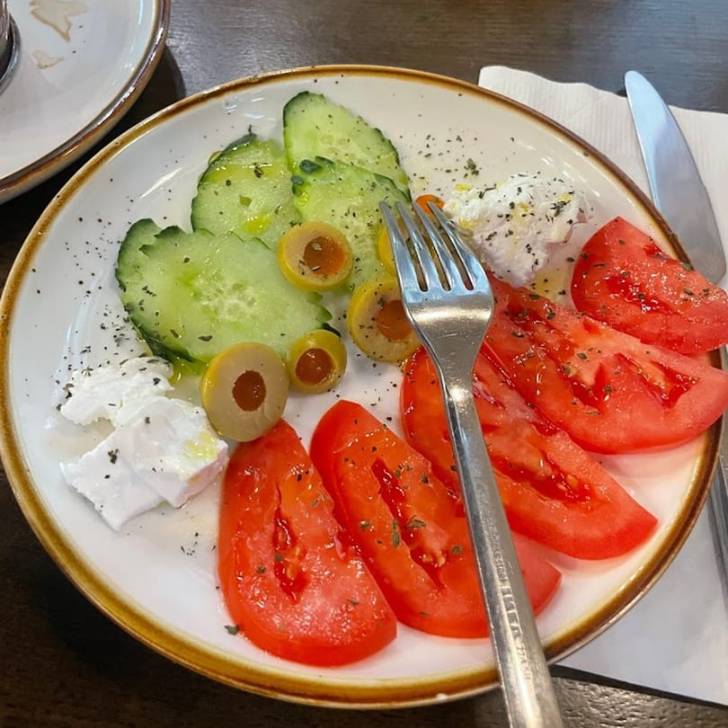A fresh Persian salad with sliced cucumbers, tomatoes, olives, and feta cheese, garnished with herbs.