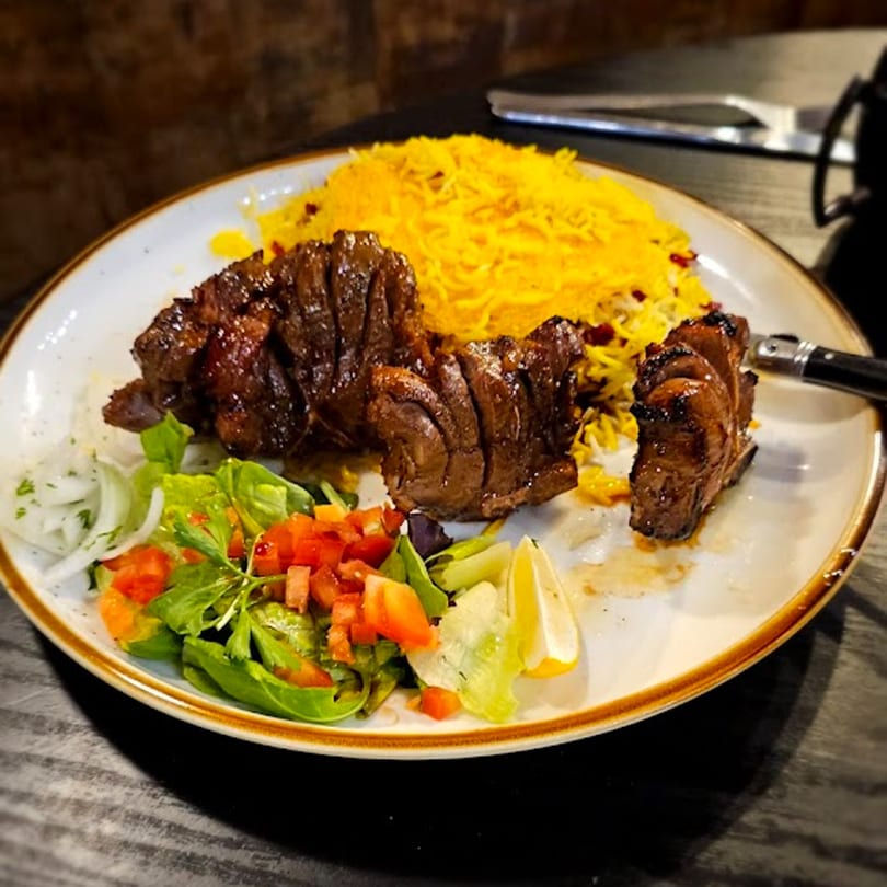 Tah Deeg Persian Cuisine's dish with grilled meat, saffron rice, and a fresh side salad.