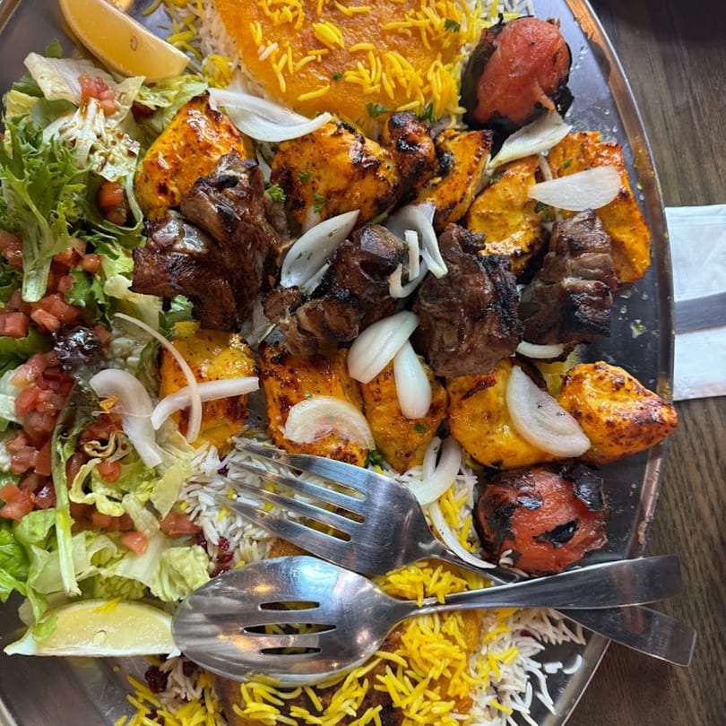 A large platter of Tah Deeg Persian cuisine with chicken and beef kebabs, rice, salad, and grilled tomatoes.