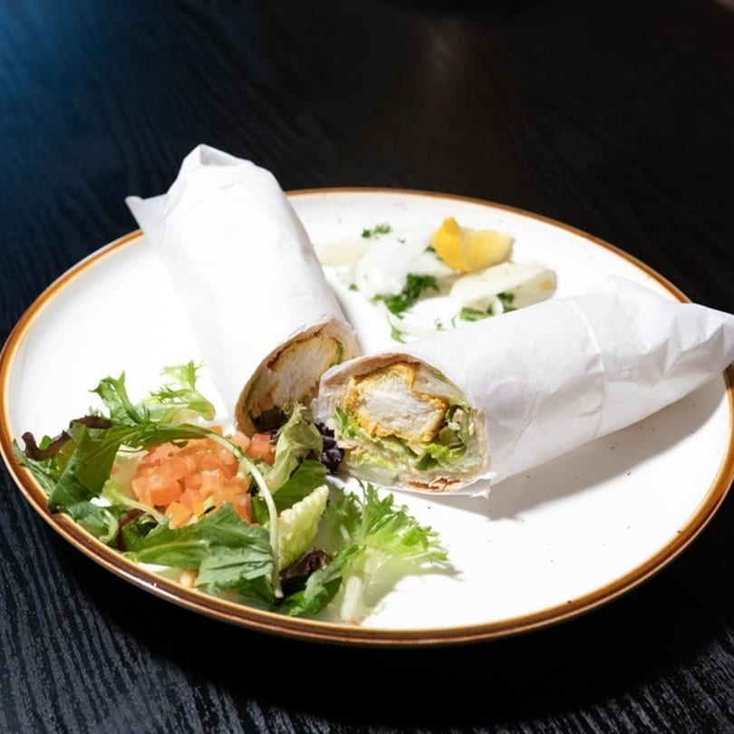 Two chicken wraps with lettuce and tomato, served with a side salad and lemon wedge.