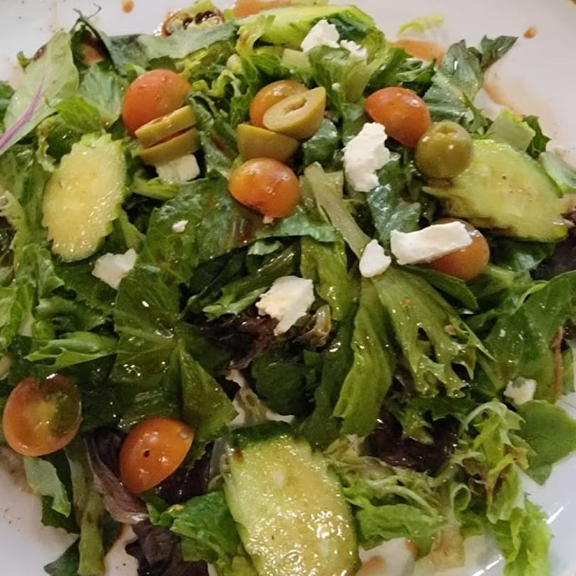 A fresh Persian salad with green lettuce, cherry tomatoes, olives, cucumbers, and feta cheese.