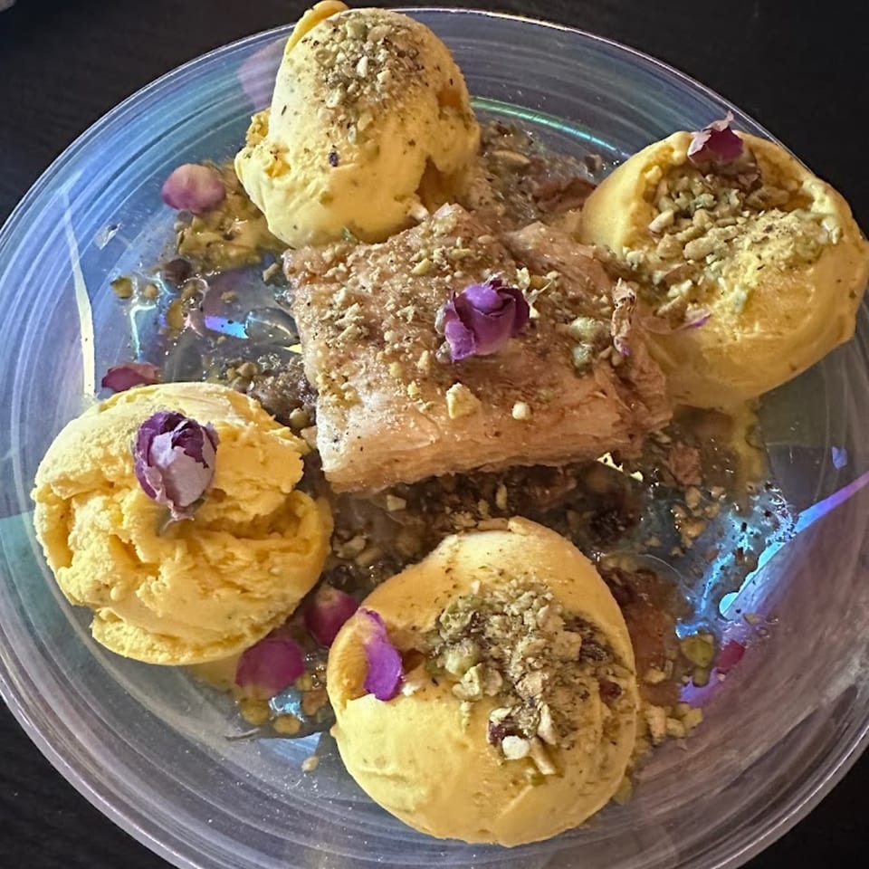 Four scoops of saffron ice cream with a piece of baklava, garnished with pistachios and rosebuds.