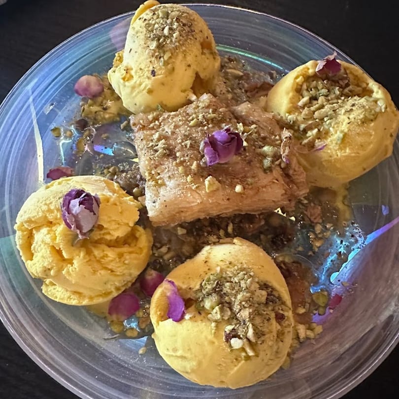 Four scoops of saffron ice cream with a piece of baklava, garnished with pistachios and rosebuds.